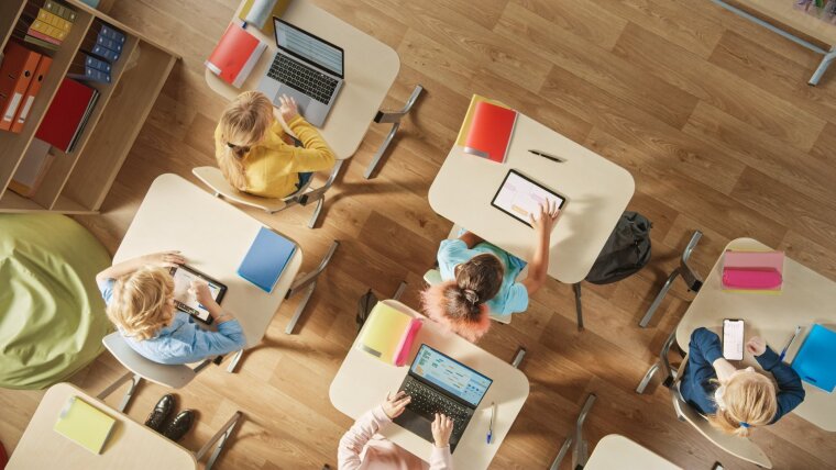 Schüler*innen benutzen digitale Geräte auf dem Schultisch (Draufsicht)